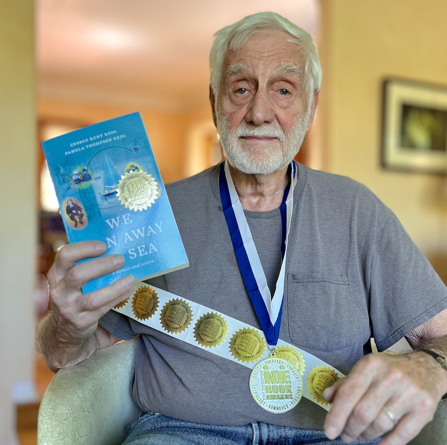 Kent holding his book, wearing the medal and showing the stickers for his Next Generation Indie Book Award for Memoir Finalist, 2025